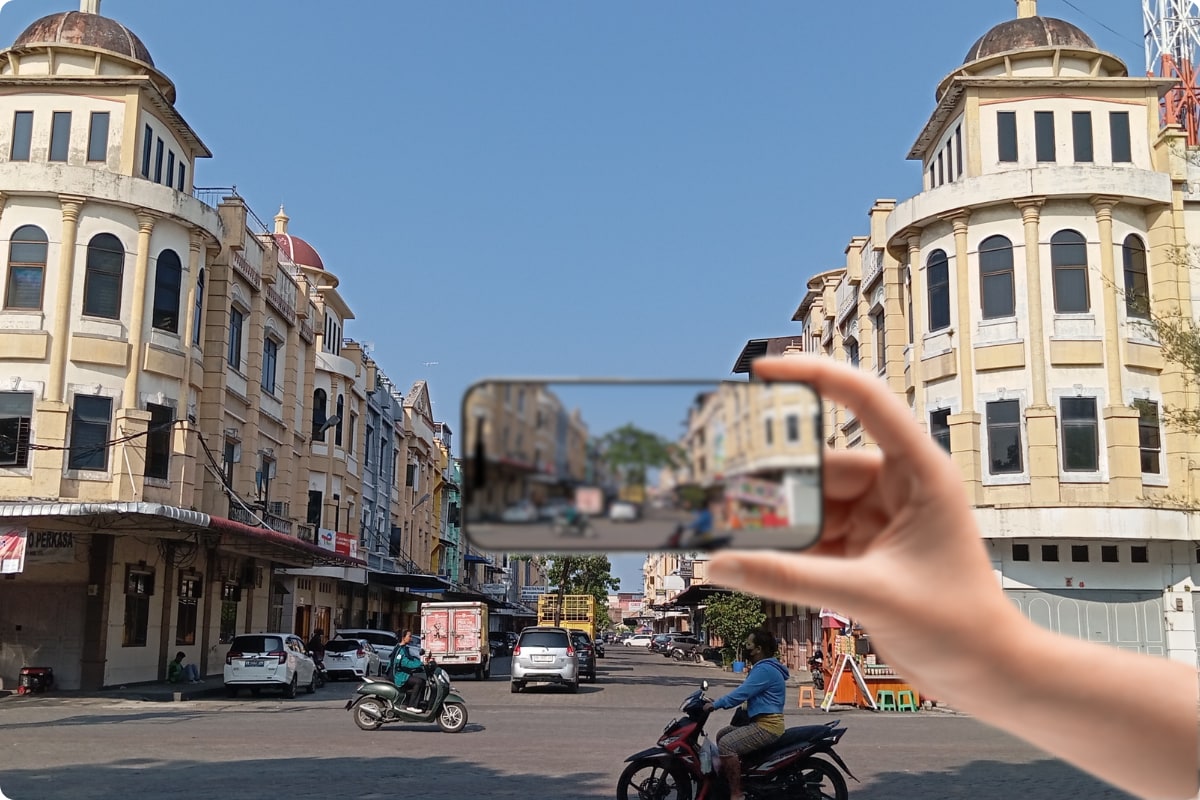 Hand holding a phone over a city street scene, with the background clear and the phone screen blurred to illustrate presbyopia vision.