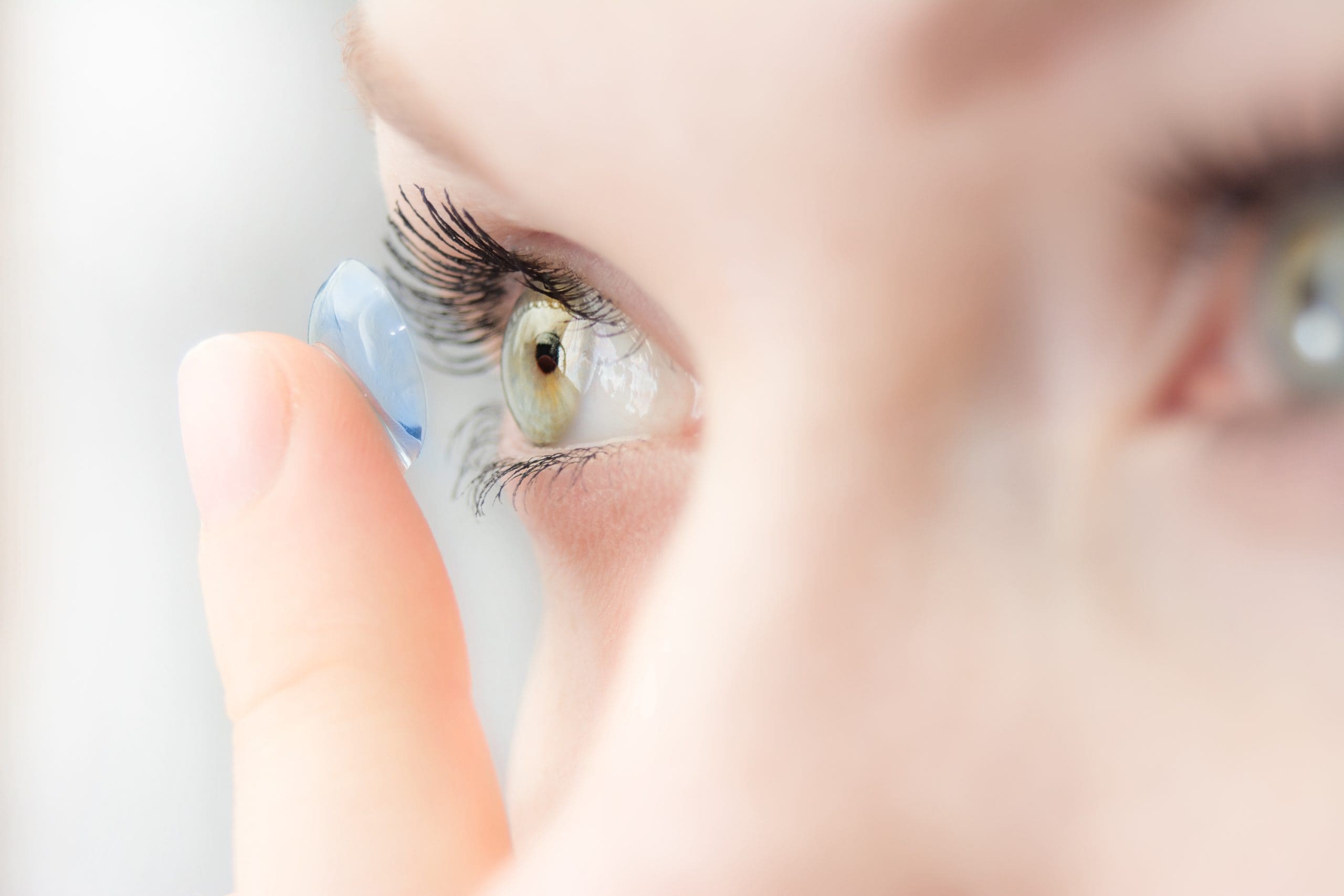 lose-up side view of a person holding a contact lens on a fingertip near the eye before insertion.