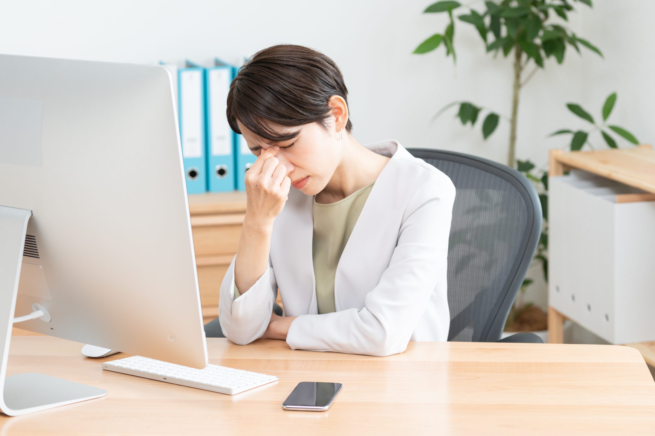 A woman sitting at her office desk rubbing her eyes in discomfort while looking at a computer monitor.