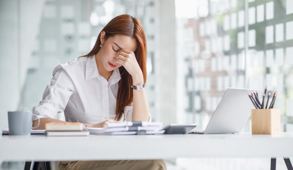 Woman experiencing eye strain and fatigue while working on a laptop at an office desk.