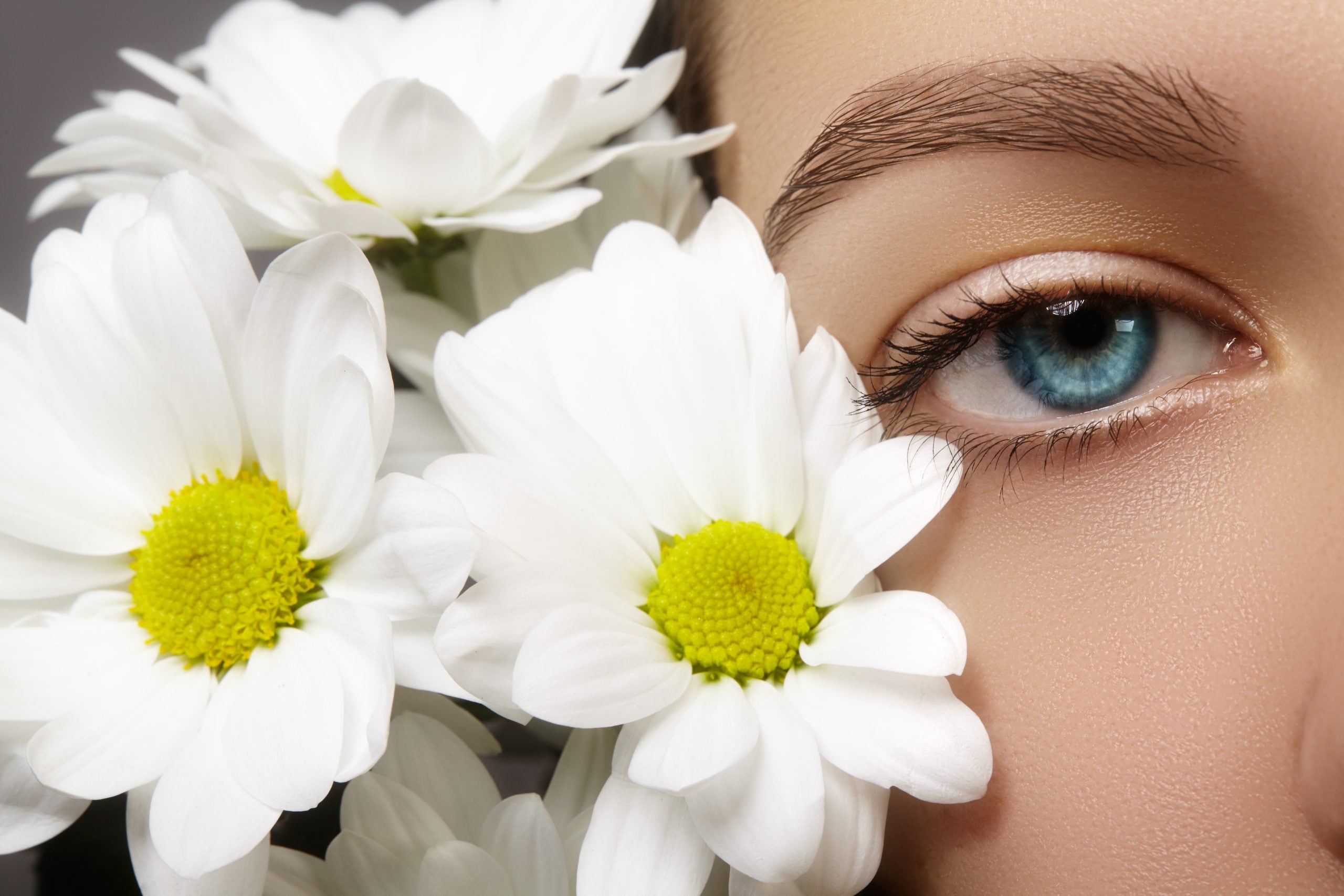 Close-up of a blue eye framed by white daisy flowers, symbolizing spring eye sensitivity and seasonal allergy discomfort.